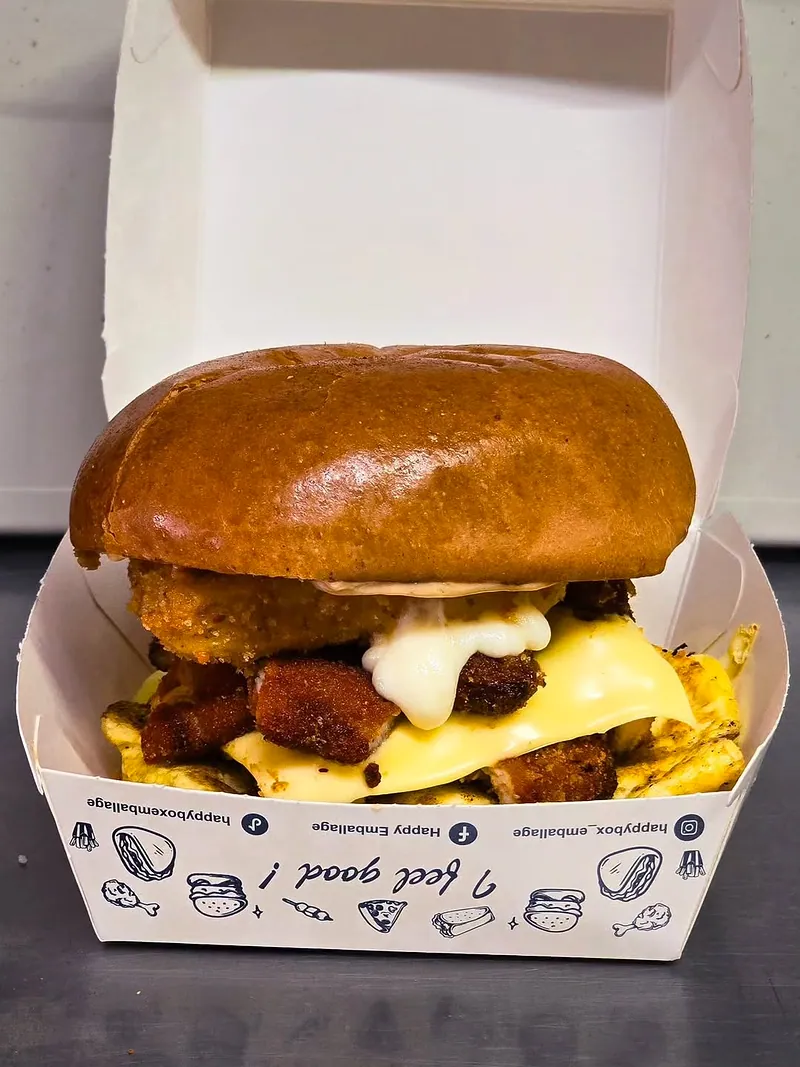 Un burger brioché garni de poulet pané croustillant, de fromage fondu et de sauce, dans sa boîte en carton