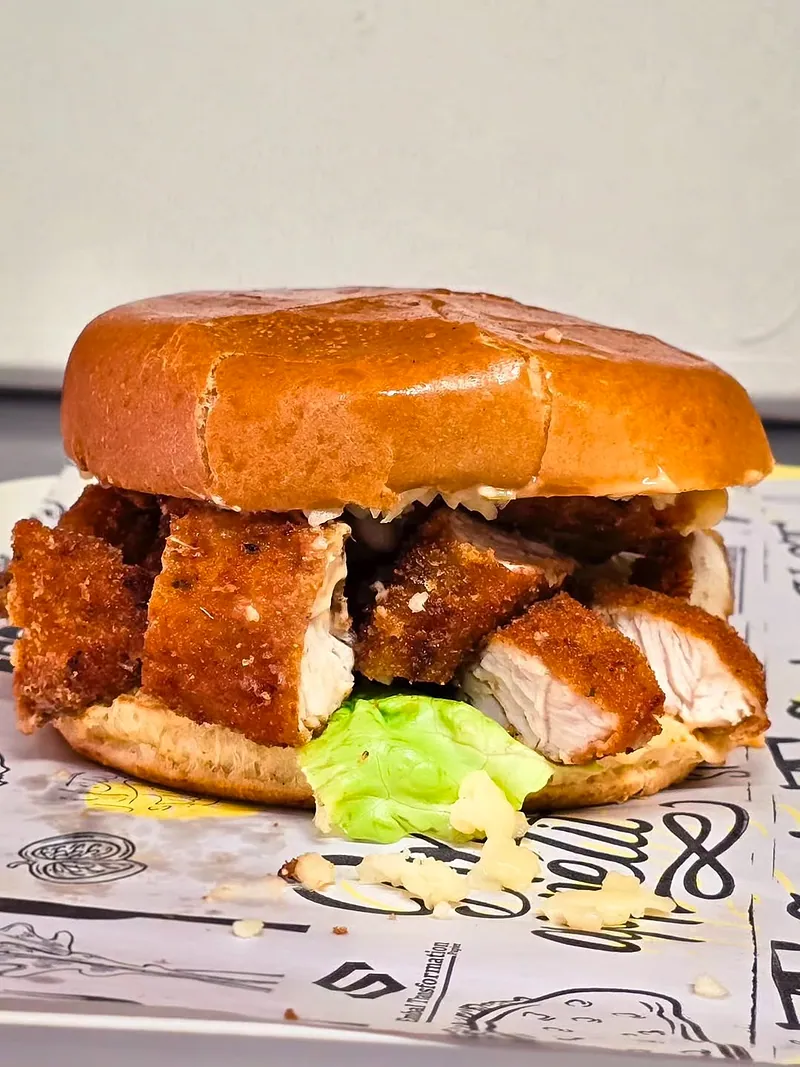 Burger brioché aux morceaux de poulet pané et à la salade, posé sur un papier imprimé